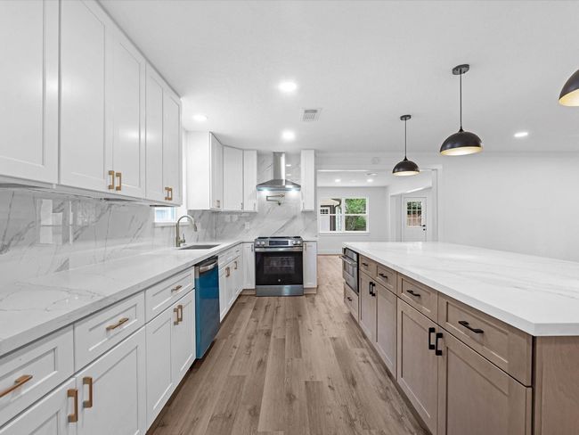 This modern kitchen features sleek white cabinetry, marble countertops, and a spacious island. It includes stainless steel appliances, wood flooring, and stylish pendant lighting, creating a bright and inviting space perfect for cooking and entertaining. | Image 12