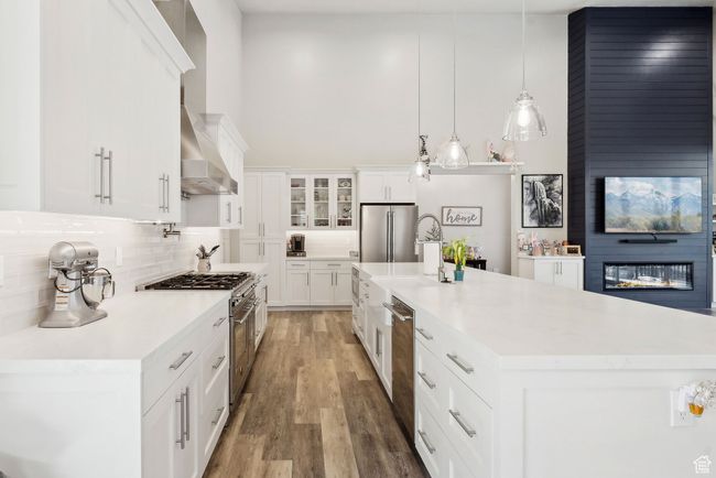 Kitchen with appliances with stainless steel finishes, light countertops, wall chimney range hood, white cabinets, and backsplash | Image 38