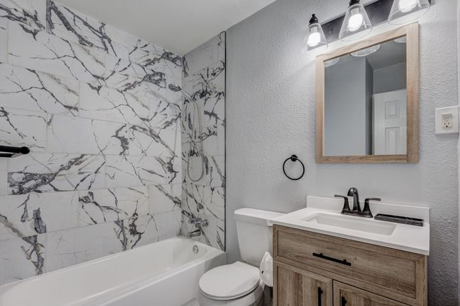 Bathroom featuring vanity, a textured wall, toilet, and shower combination | Image 8