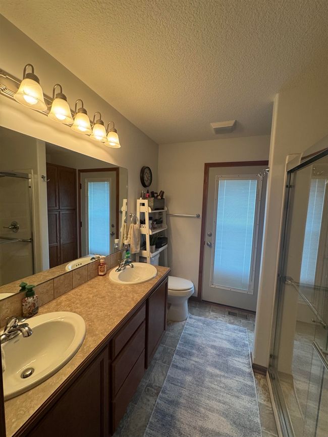 Bathroom with a shower stall, toilet, a textured ceiling, and double vanity | Image 21