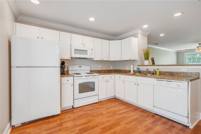 Kitchen with white appliances, a sink, white cabinetry, light wood-type flooring, and crown molding | Image 4