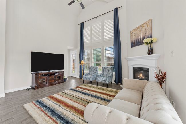 Living area featuring a high ceiling, ceiling fan, wood finished floors, a glass covered fireplace, and baseboards | Image 17