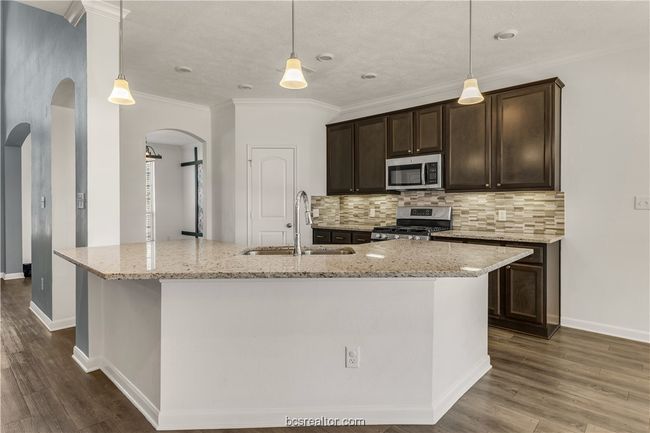 Kitchen featuring sink, appliances with stainless steel finishes, hanging light fixtures, light stone countertops, and an island with sink | Image 8