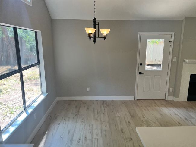 Unfurnished dining area with a chandelier, healthy amount of natural light, light wood finished floors, lofted ceiling, and a fireplace | Image 6