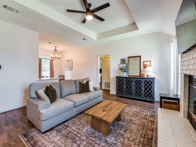 Living room featuring a fireplace, a ceiling fan, wood finished floors, a chandelier, and a raised ceiling | Image 9