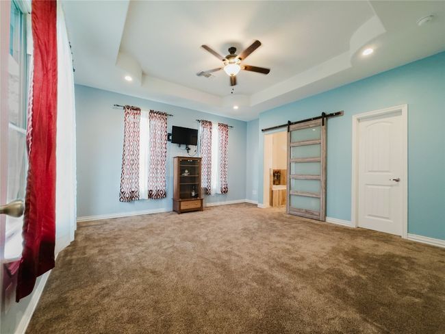 Unfurnished bedroom with a tray ceiling, carpet flooring, a barn door, recessed lighting, and a ceiling fan | Image 17