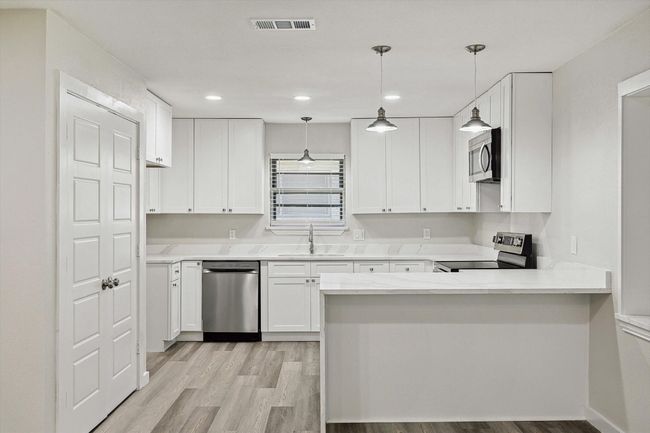Kitchen with appliances with stainless steel finishes, a sink, white cabinetry, visible vents, and a peninsula | Image 10