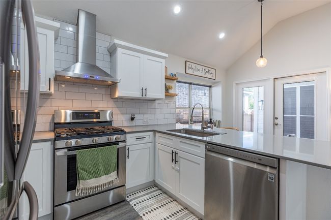 Kitchen featuring stainless steel appliances, a sink, wall chimney range hood, decorative backsplash, and hanging light fixtures | Image 13