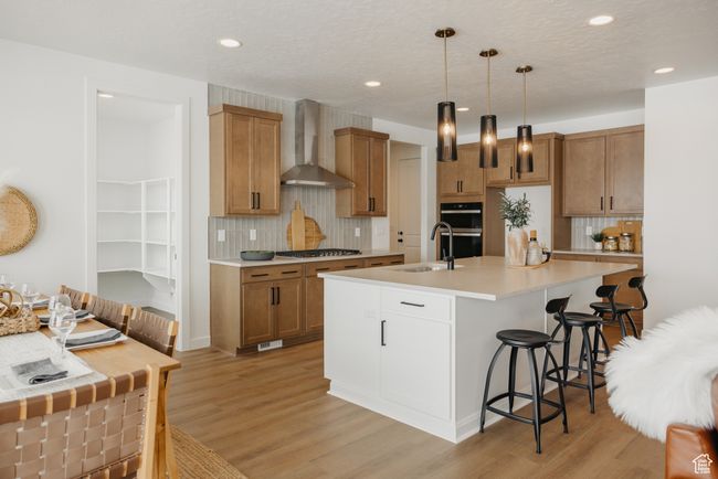 Kitchen featuring wall chimney range hood, a sink, a breakfast bar area, decorative backsplash, and recessed lighting | Image 14