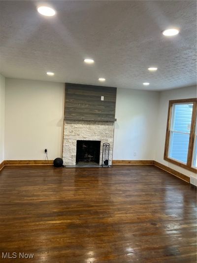 Unfurnished living room featuring a textured ceiling, a fireplace, and dark hardwood / wood-style flooring | Image 3