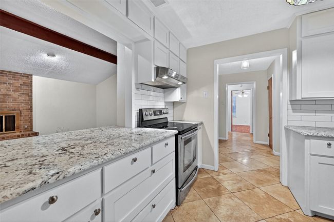 Kitchen with stainless steel range with electric cooktop, exhaust hood, tasteful backsplash, light tile patterned floors, and white cabinets | Image 7