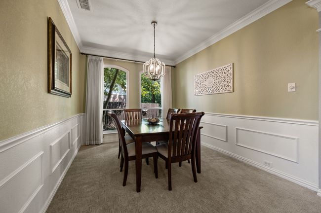 Carpeted dining space with a decorative wall, a wainscoted wall, crown molding, a chandelier, and a textured wall | Image 8