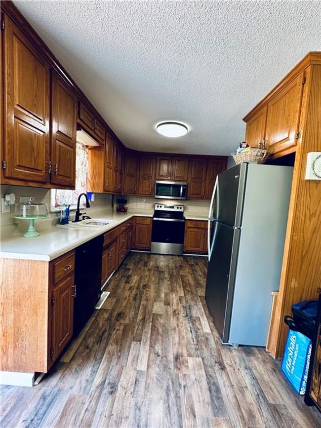 Kitchen featuring stainless steel appliances, a sink, a textured ceiling, dark wood finished floors, and light countertops | Image 11