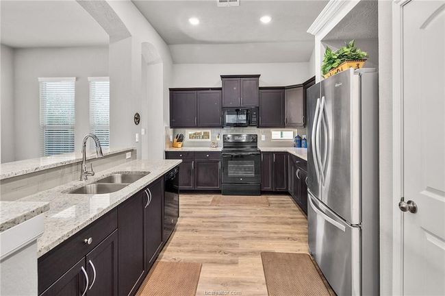 Kitchen with light stone counters, dark brown cabinetry, sink, black appliances, and light hardwood / wood-style flooring | Image 7