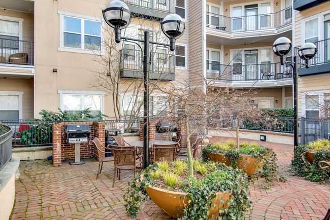 Relax or entertain in this charming courtyard common area featuring brick pathways, lush planters, cozy seating, and a built-in grill—perfect for casual outdoor gatherings. | Image 18