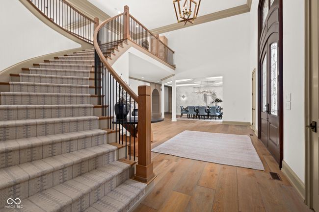 foyer featuring a towering ceiling, stairway, baseboards, a chandelier, and wood finished floors | Image 7