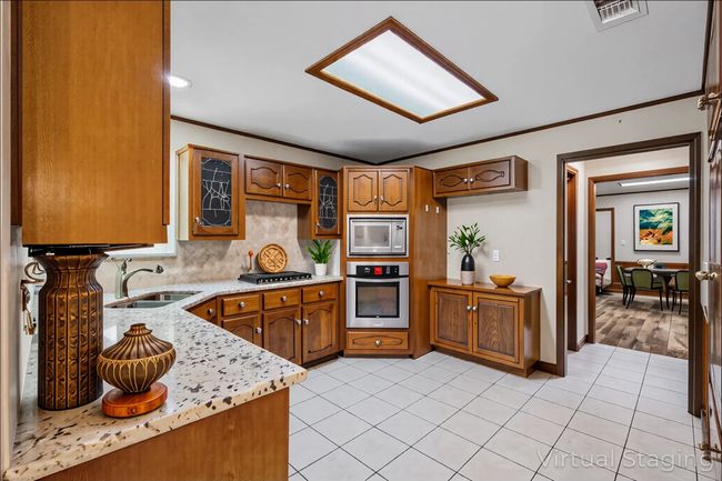Kitchen with appliances with stainless steel finishes, a sink, brown cabinets, crown molding, and light tile patterned floors | Image 12