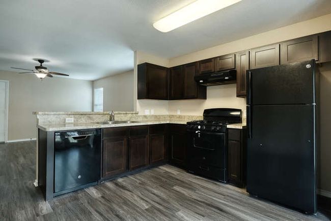 Kitchen with black appliances, ventilation hood, dark brown cabinets, dark wood finished floors, and ceiling fan | Image 5