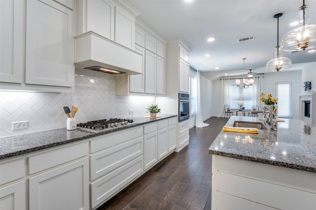 Kitchen featuring a kitchen island, a sink, white cabinetry, hanging light fixtures, and appliances with stainless steel finishes | Image 5