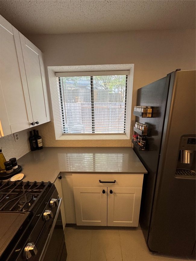 Kitchen featuring refrigerator, stove, white cabinetry, a textured ceiling, and light tile patterned floors | Image 6