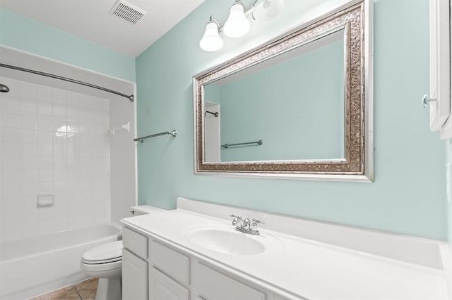 This full bath features a tub/shower combination with crisp white tile surround. A wide vanity with ample counter space is accented by a decorative framed mirror and updated lighting. | Image 19