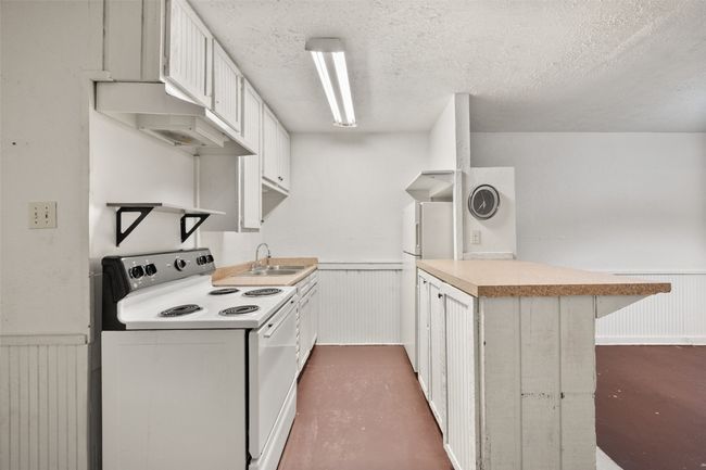 Kitchen with a wainscoted wall, a peninsula, white appliances, and white cabinets | Image 7