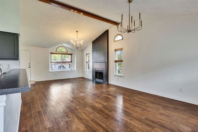 Unfurnished living room featuring dark wood-style floors, beamed ceiling, a chandelier, a tiled fireplace, and high vaulted ceiling | Image 5