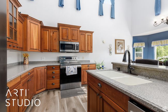 Kitchen with appliances with stainless steel finishes, a sink, a high ceiling, light wood finished floors, and glass insert cabinets | Image 12