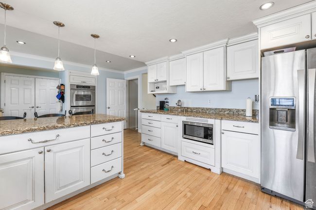 Kitchen with light wood finished floors, white cabinets, ornamental molding, stainless steel appliances, and pendant lighting | Image 12