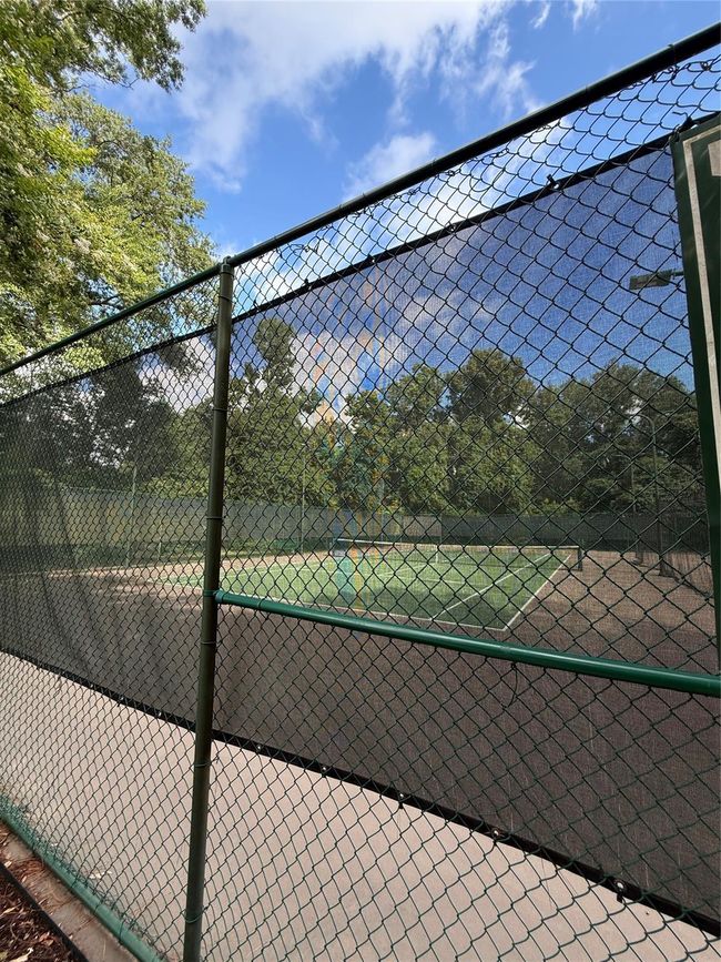 This photo features a fenced tennis court surrounded by trees, offering a recreational space in a natural setting. | Image 39