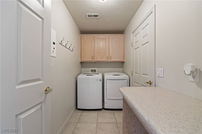 Laundry room featuring cabinet space, washing machine and dryer, light tile patterned floors, and a textured ceiling | Image 22