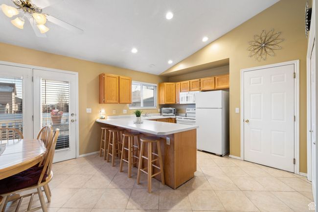 Kitchen featuring light tile patterned floors, white appliances, a breakfast bar area, vaulted ceiling, and kitchen peninsula | Image 9