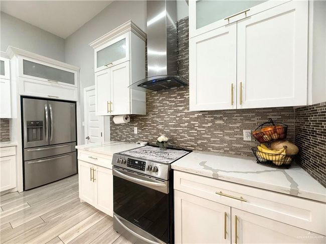 Kitchen featuring stainless steel appliances, wall chimney range hood, backsplash, light stone counters, and light wood-style floors | Image 6