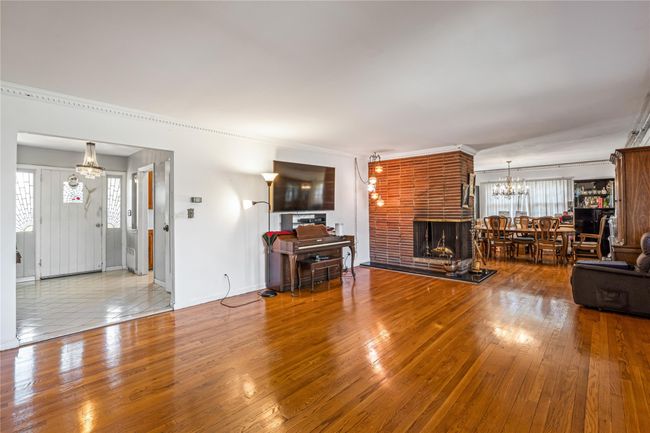Unfurnished living room with wood-type flooring, a notable chandelier, baseboards, and a fireplace | Image 11