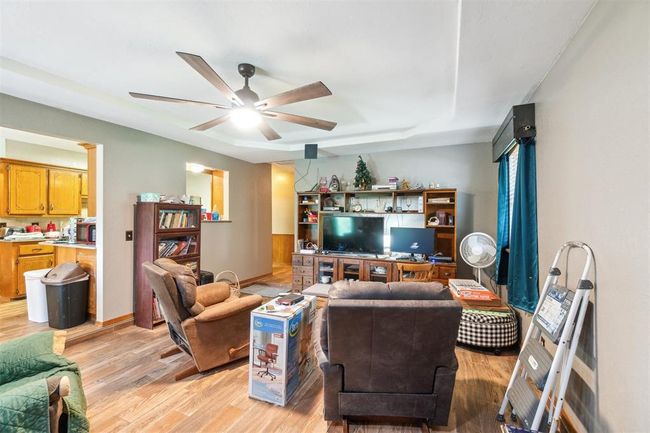 Living area with a ceiling fan, light wood-style floors, and a tray ceiling | Image 10