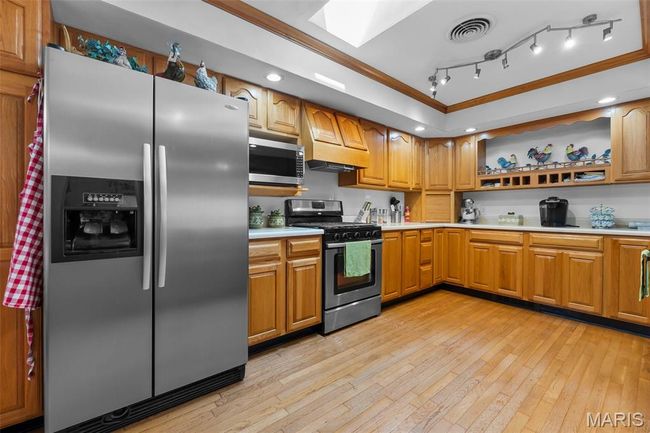 Kitchen featuring stainless steel appliances, crown molding, light countertops, open shelves, and light wood-style flooring | Image 66