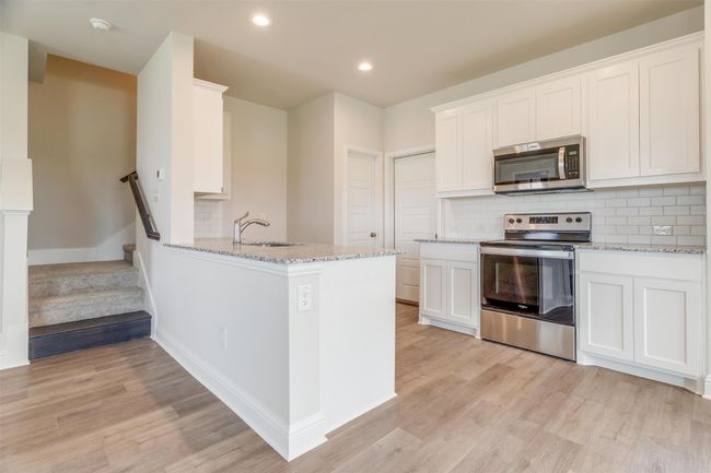 Kitchen with sink, white cabinetry, kitchen peninsula, stainless steel appliances, and backsplash | Image 12