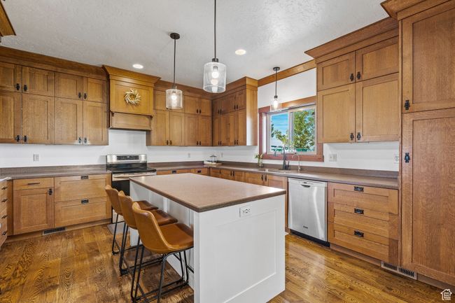Kitchen with dark wood-type flooring, hanging light fixtures, a kitchen island, stainless steel appliances, and a kitchen bar | Image 15