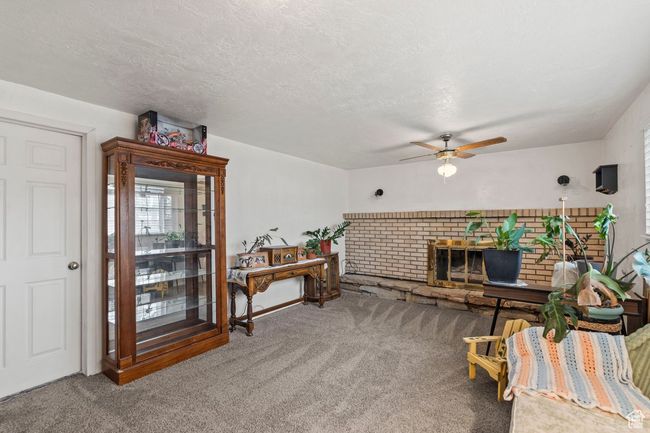 Living area featuring a textured ceiling, ceiling fan, carpet floors, and a fireplace | Image 22
