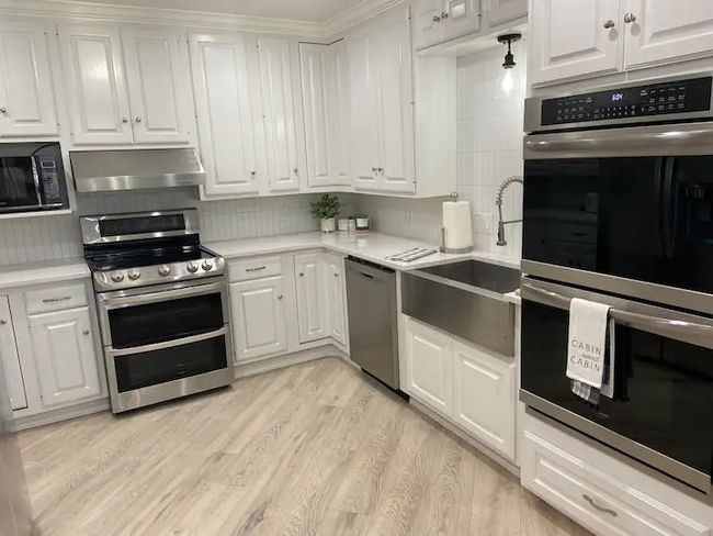 Kitchen with ventilation hood, white cabinetry, sink, and stainless steel appliances | Image 6