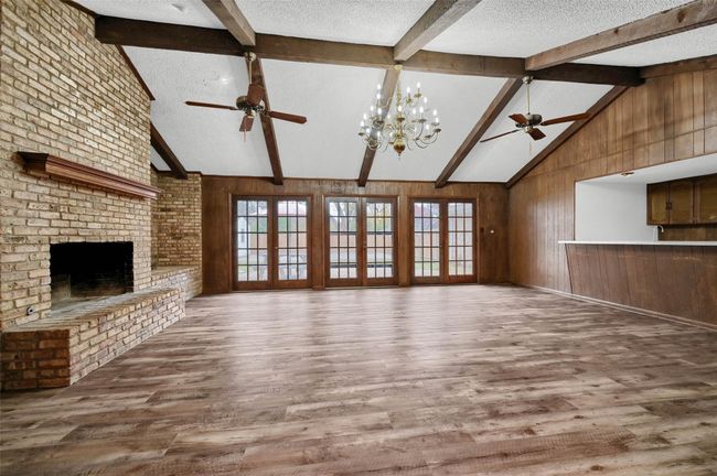 Unfurnished living room featuring ceiling fan, wood finished floors, wood walls, a brick fireplace, and a textured ceiling | Image 6