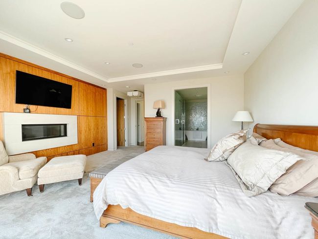 Bedroom featuring light carpet, a tray ceiling, a glass covered fireplace, and ensuite bathroom | Image 33