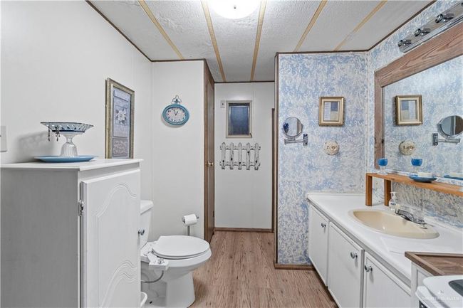 Bathroom featuring a textured ceiling, wood finished floors, toilet, vanity, and wallpapered walls | Image 9