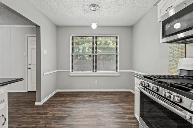 Kitchen featuring stainless steel appliances, dark wood finished floors, a textured ceiling, white cabinetry, and baseboards | Image 7
