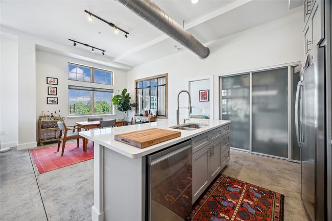 Kitchen featuring finished concrete flooring, gray cabinets, light countertops, dishwashing machine, and freestanding refrigerator | Image 12