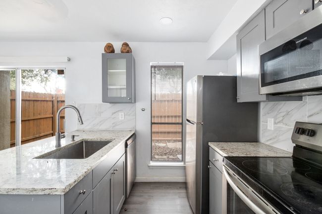 Kitchen featuring backsplash, sink, light stone countertops, gray cabinetry, and stainless steel appliances | Image 8
