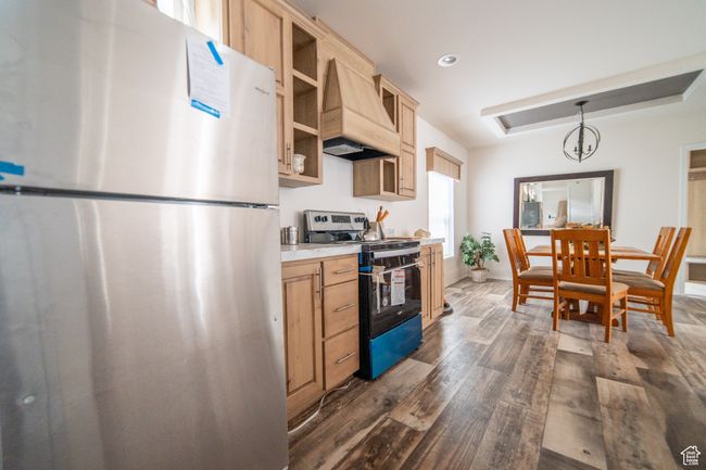 Kitchen featuring stainless steel appliances, light brown cabinetry, dark wood-style flooring, light countertops, and premium range hood | Image 60