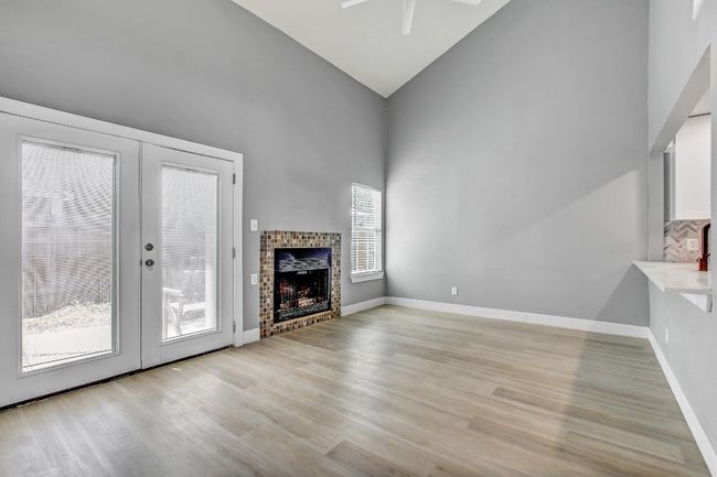 Unfurnished living room with high vaulted ceiling, ceiling fan, light wood-style floors, french doors, and a fireplace | Image 4