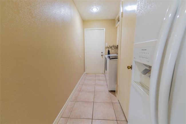 This photo shows the laundry room with tiled flooring and beige walls. The space is well-lit with a ceiling light and has a door leading outside to the garage. | Image 18
