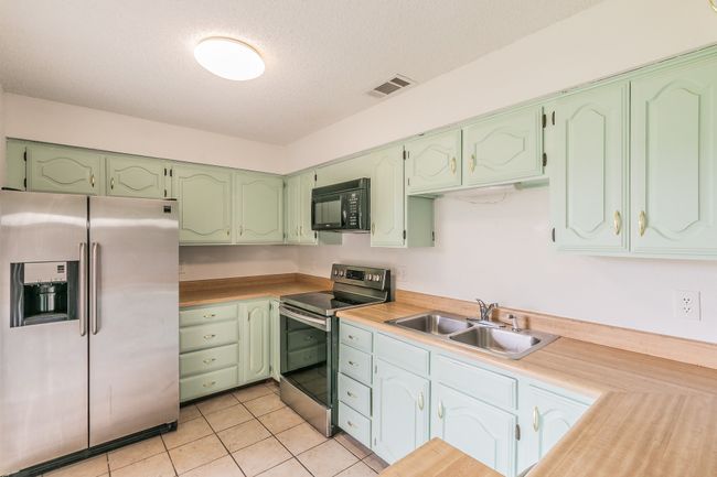 Kitchen featuring stainless steel appliances, a sink, a textured ceiling, light tile patterned flooring, and light countertops | Image 7